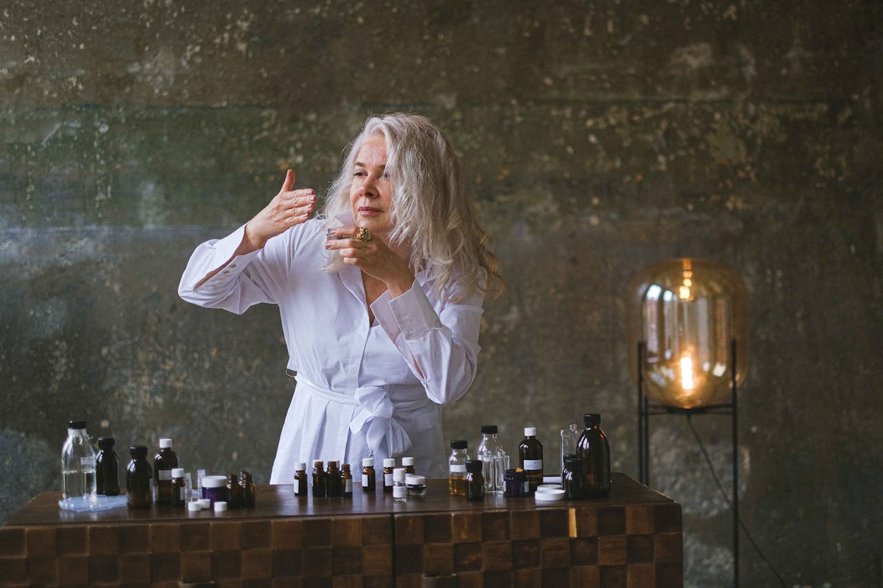 Senior woman crafting natural cosmetics in a rustic setting, surrounded by bottles and mixing ingredients.